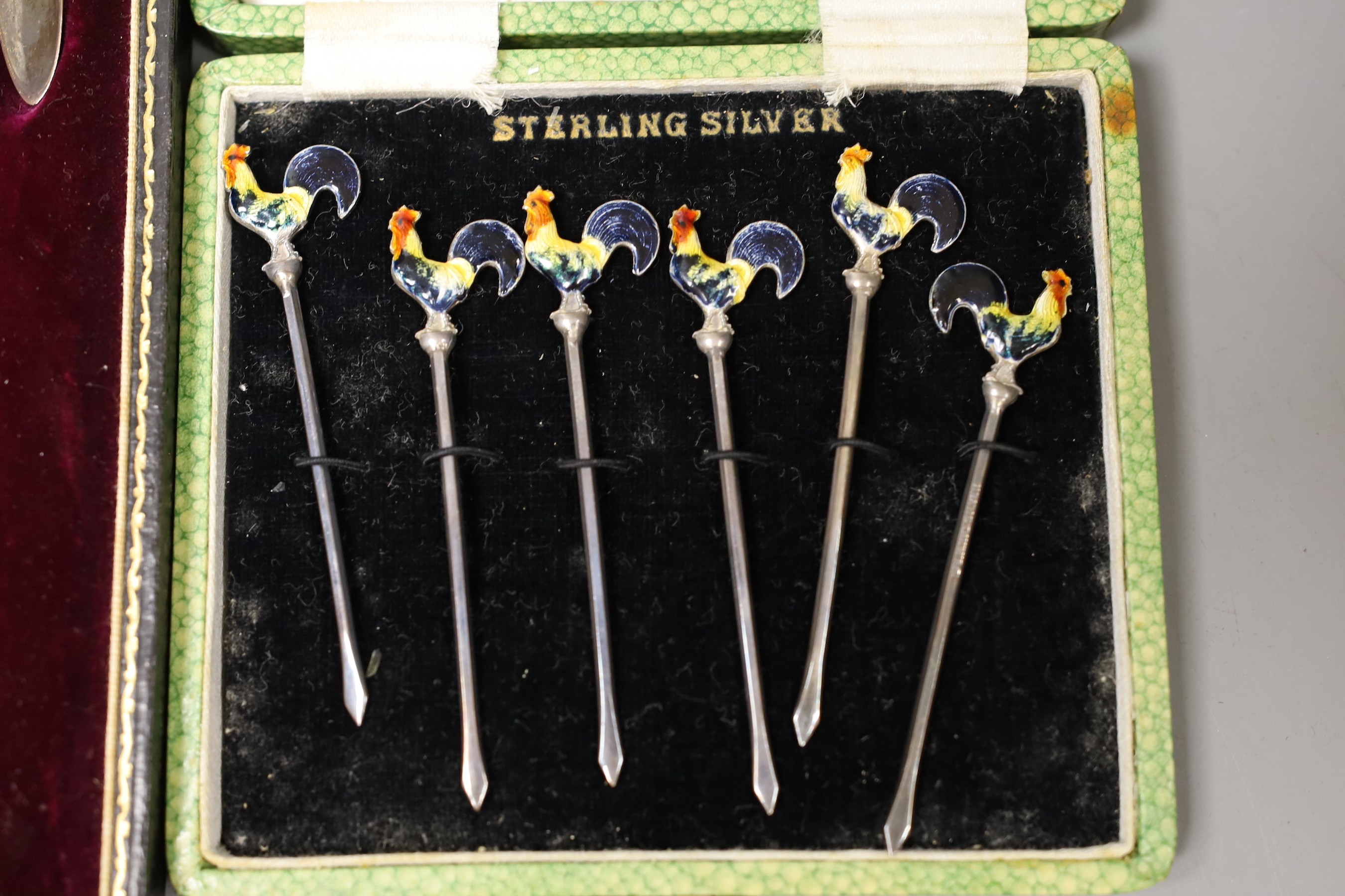 A George V cased set of six silver lobster picks and plated crackers and a similar set of silver and enamel cocktail sticks